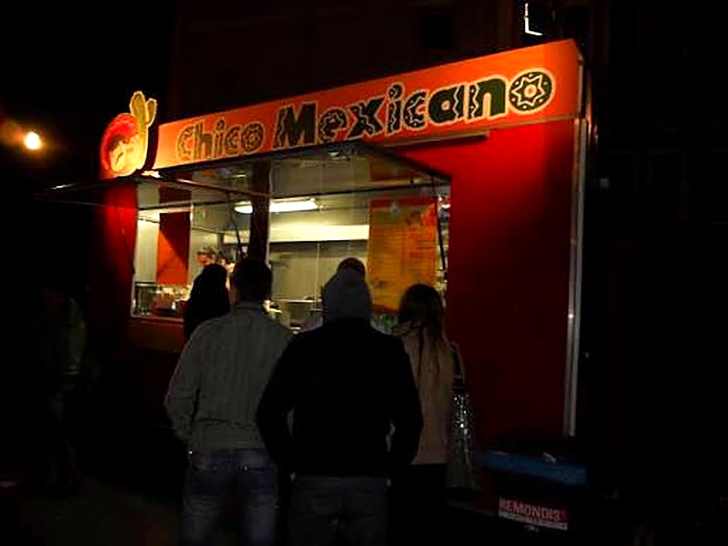 Budka Chico Mexicano wieczorem — kolejka klientów przed podświetlonym okienkiem